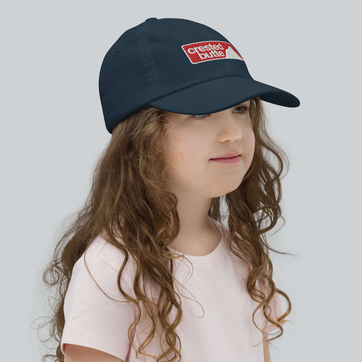 Crested Butte Youth Baseball Cap worn by a girl, showcasing Mtns Co official licensed ski resort apparel.