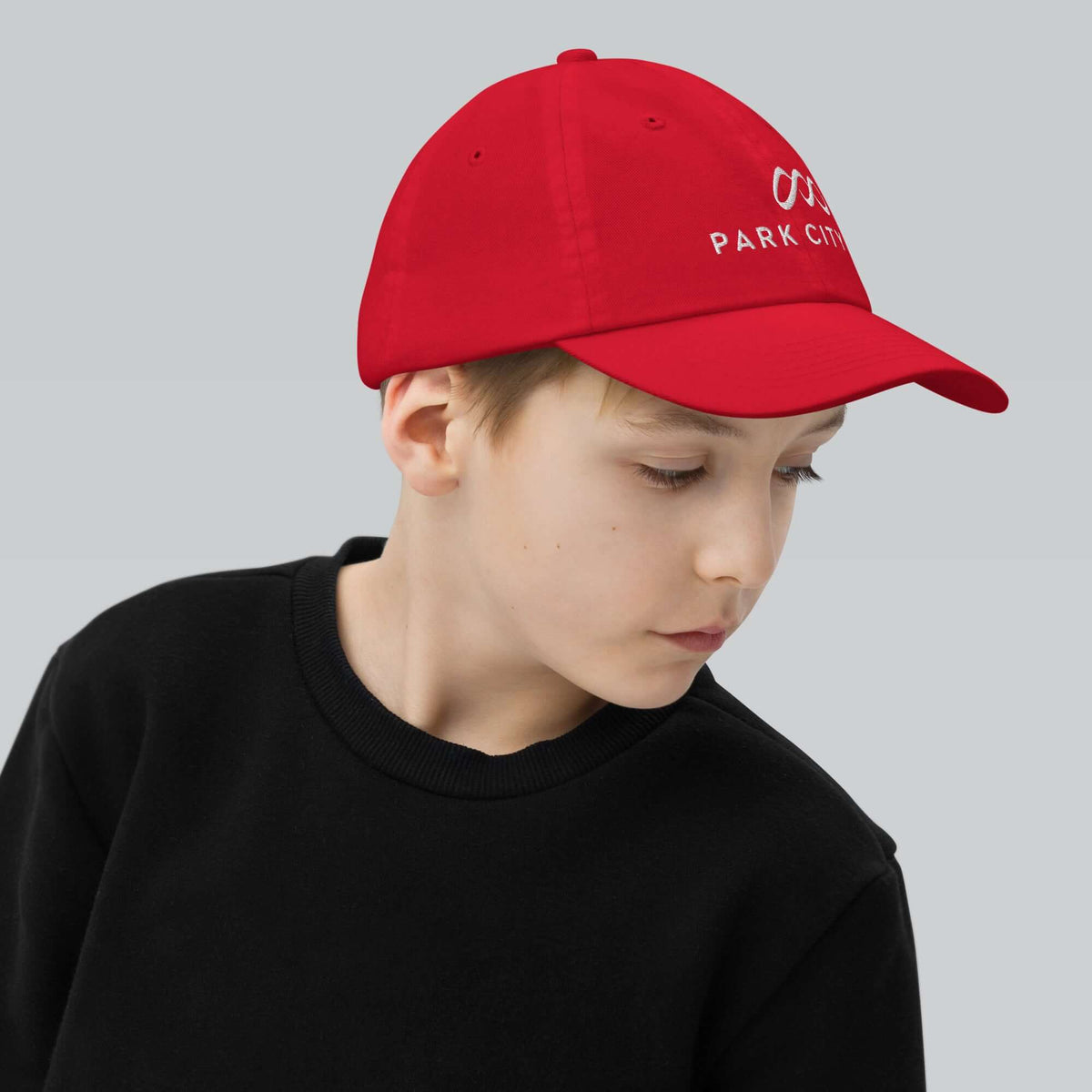 Park City Youth Baseball Cap worn by a child showcasing Mtns Co Trail Map Logo, perfect for sunny days outdoors.