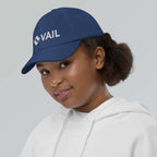 Vail Youth Baseball Cap on a smiling girl, featuring Mtns Co Trail Map Logo, official licensed ski resort apparel.