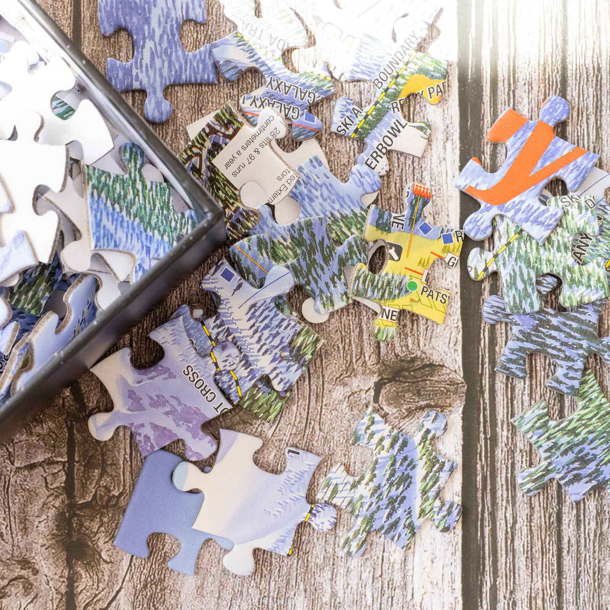 Colorful pieces of the Heavenly Ski Resort Jigsaw Puzzle – 500 Pieces scattered on a wooden surface by Mtns Co.